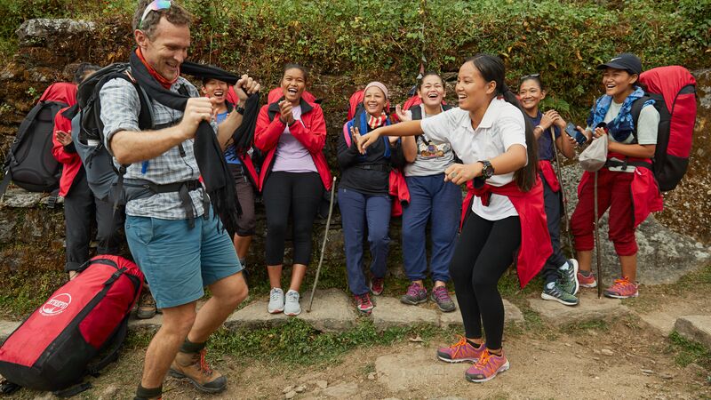 A trekker dances on the trail with a female porter