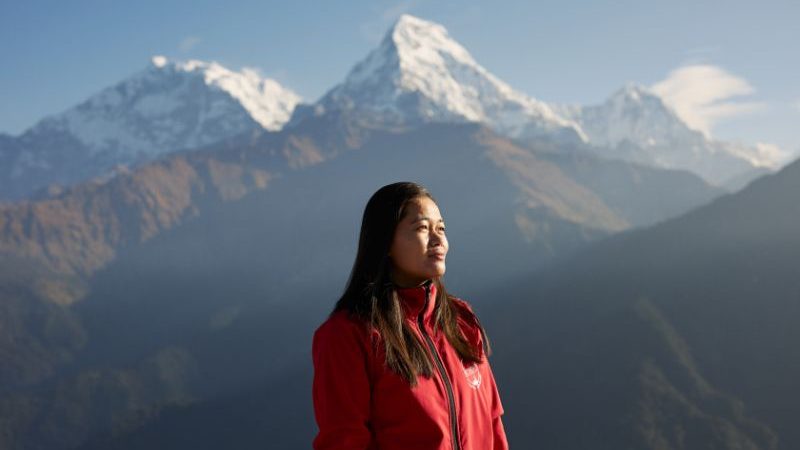 A woman wearing a red jacket with mountains in the background