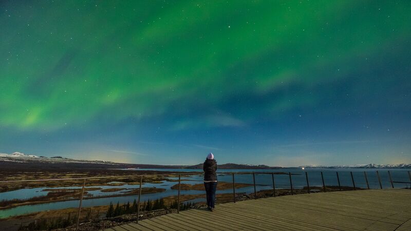 A solo traveller gazes at the swirling blues and greens of the Aurora Borealis.
