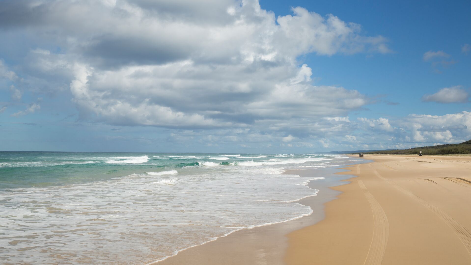 A wide view of 75 Mile Beach with two cars on the sand