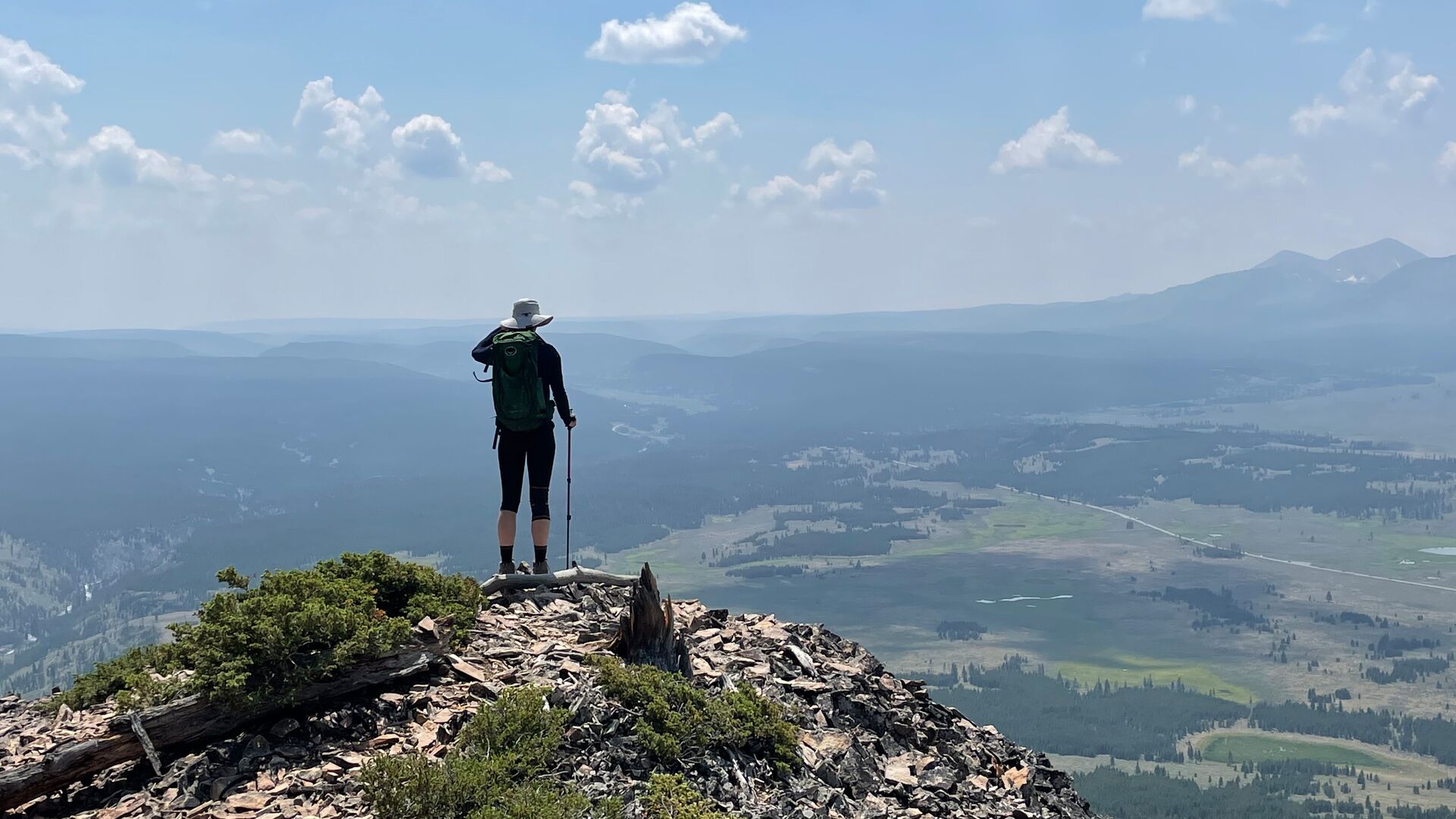 A solo traveller stands at a viewpoint on a hike in Yellowstone looking down into the valley.