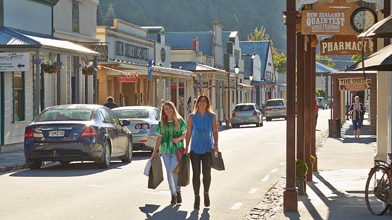 Two women walking down the main street of Arrowtown carrying shopping bags.