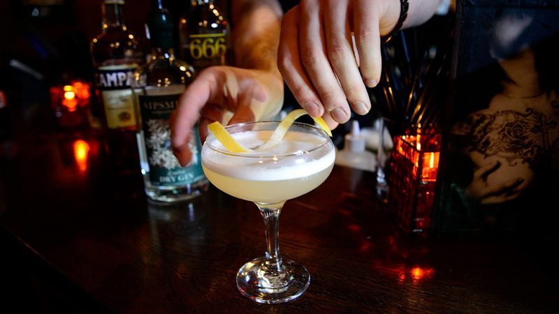 A cocktail being finished with a garnish of lemon peel.