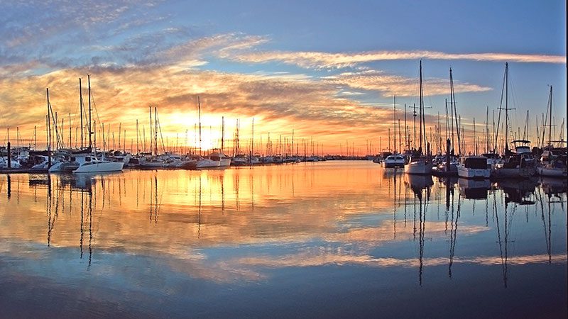 The setting sun is reflected on the water surrounded by boats in Manly Harbour in Brisbane.
