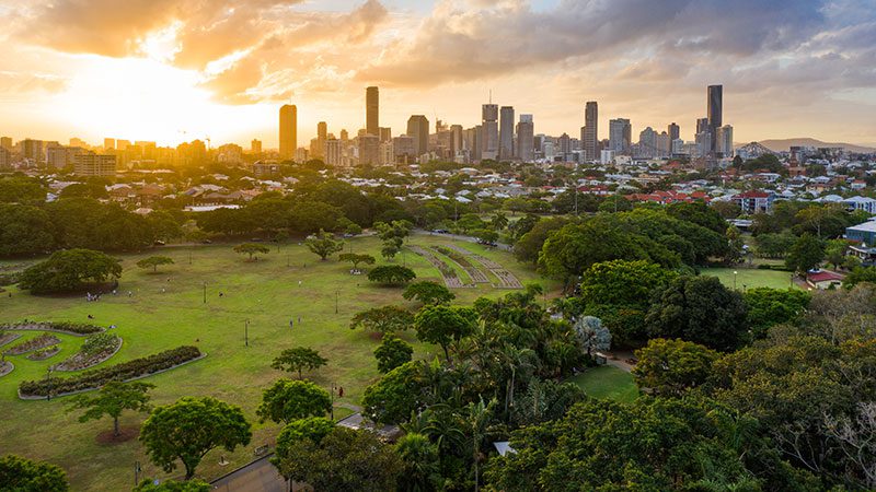 An aerial view of New Farm Park at sunset with Brisbane city in the background.