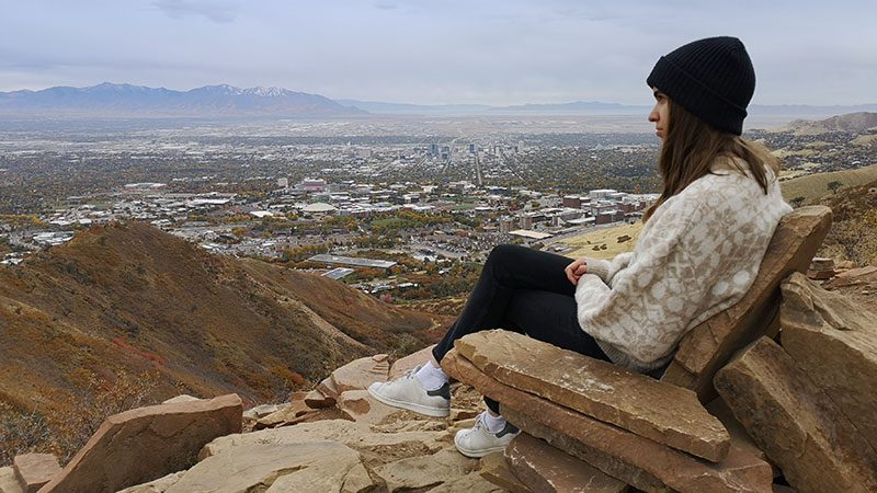 A woman sitting in a seat-like rock formation at the top of the Living Room Hike in Salt Lake City.