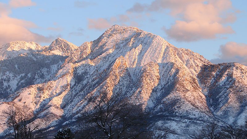 A snow-capped Mt. Olympus in Salt Lake City beneath a setting sun. 