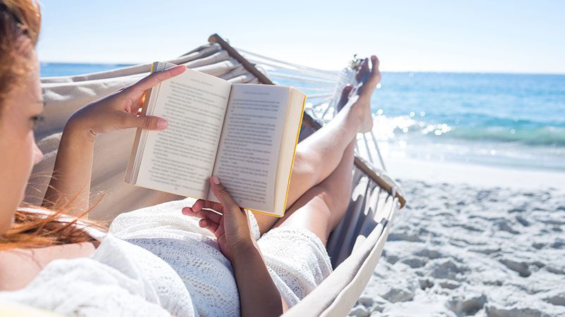woman sitting in a hammock reading on the beach