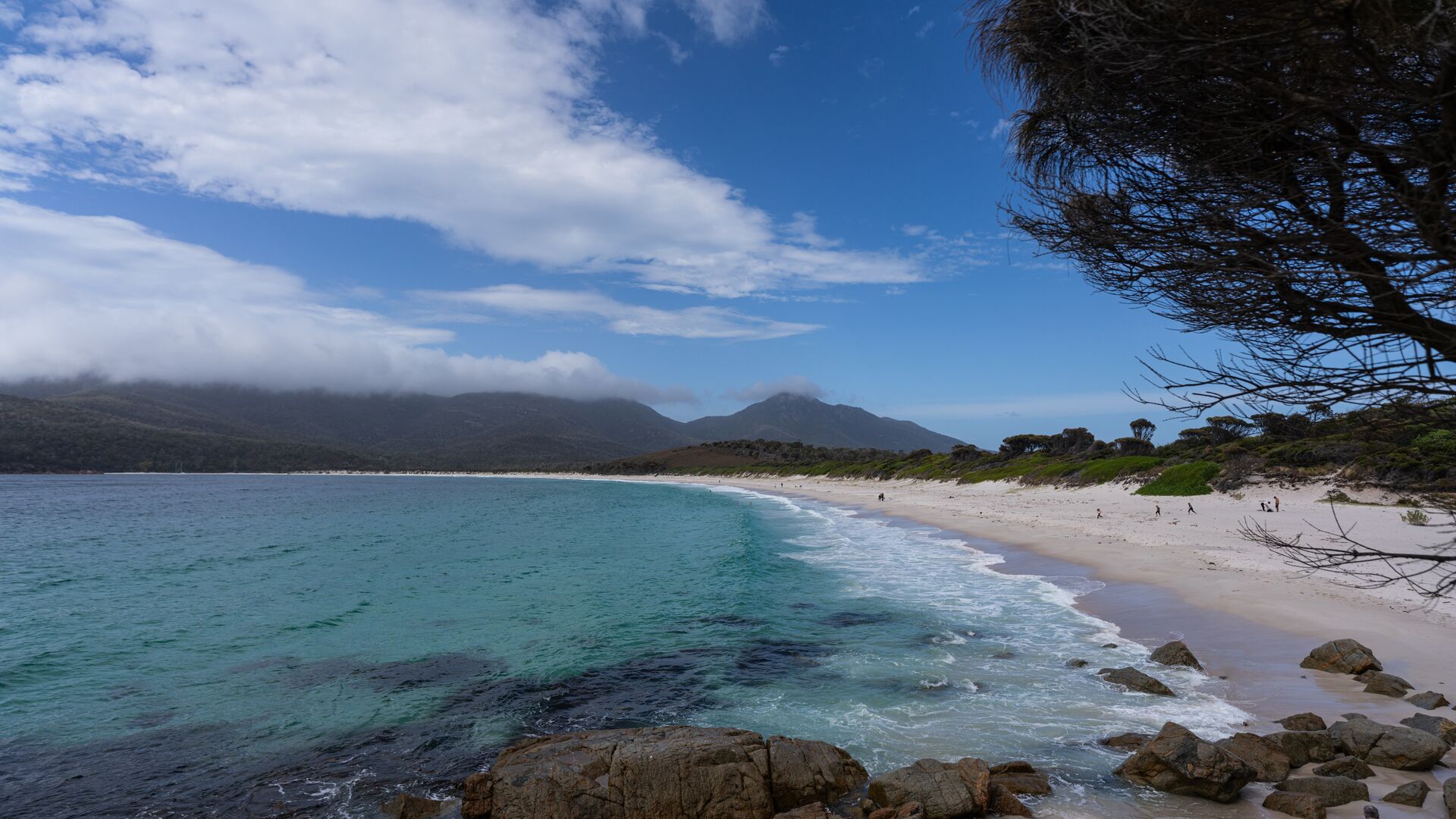 Wineglass Bay from the water with people running along sand.