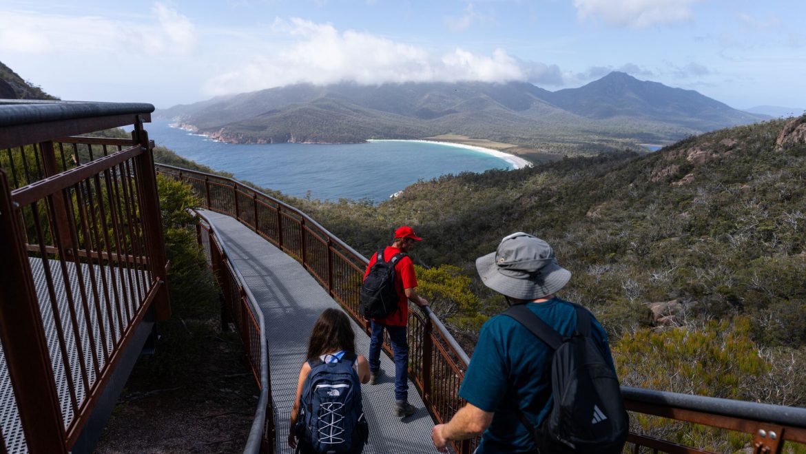 An Intrepid leader and travellers walk across a boardwalk overlooking Wineglass Bay