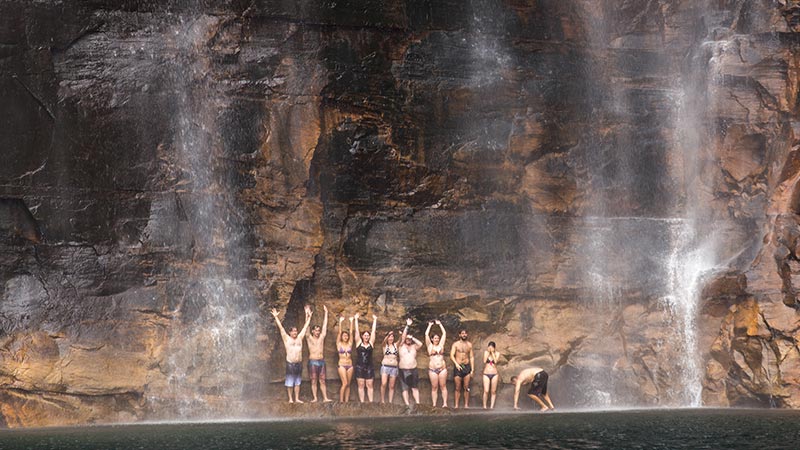 A group of travellers standing under the water of Jim Jim Falls.