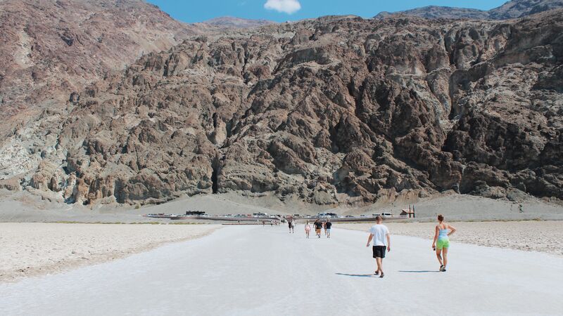 A group of travelers walking towards a rocky cliff face in Death Valley National Park.