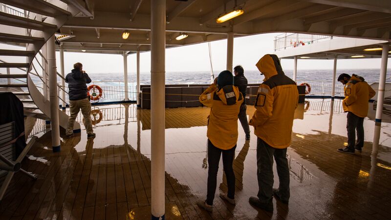 A group of people standing on the deck on an Antarctic ship while crossing the Drake Passage.