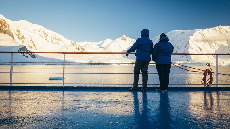 Two travellers standing on the deck of a ship looking out at an icy landscape