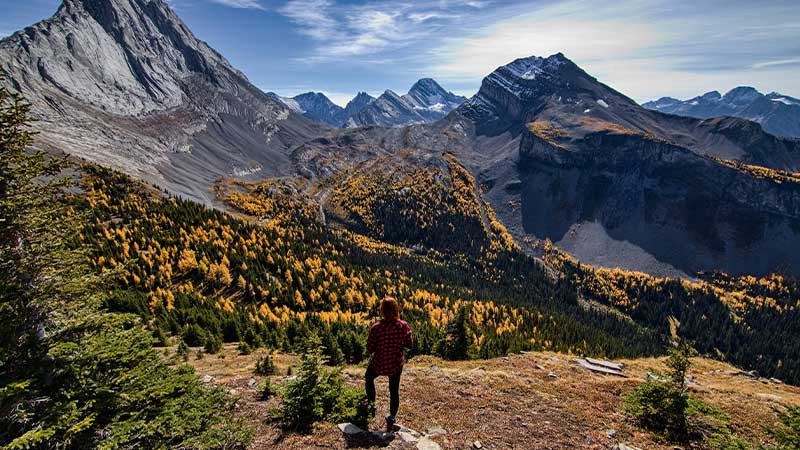 Traveller standing on a rocky outcrop looking out at the mountain landscape of the Canadian Rockies.