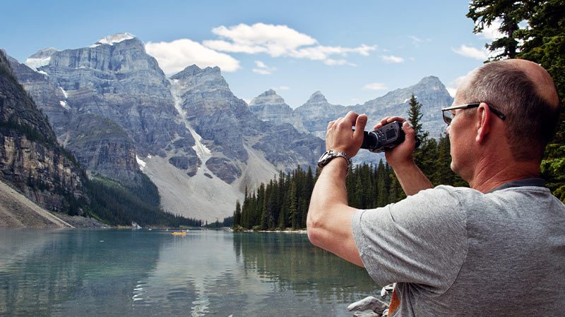 Traveller taking video footage of the 10 peaks above an emerald green lake. 