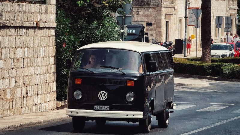 A black VW Kombi driving up a road