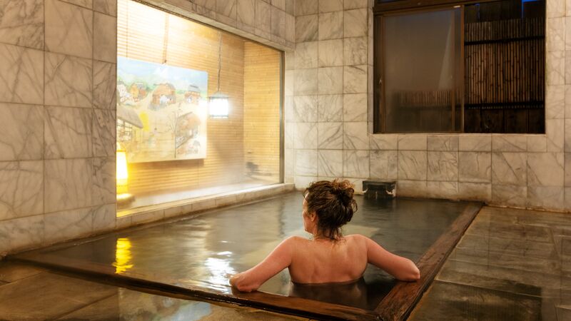 Woman relaxing in the mineral waters of natural indoor onsen pool. 