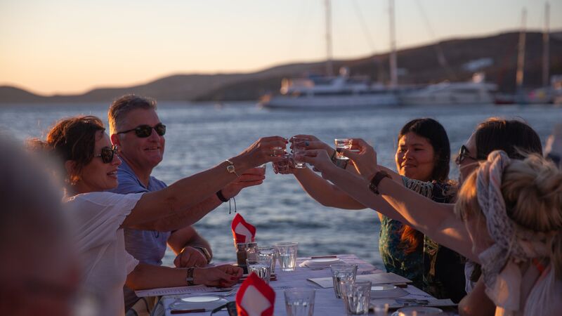A group of travelers raise a bowl of shot glasses filled with ouzo. 