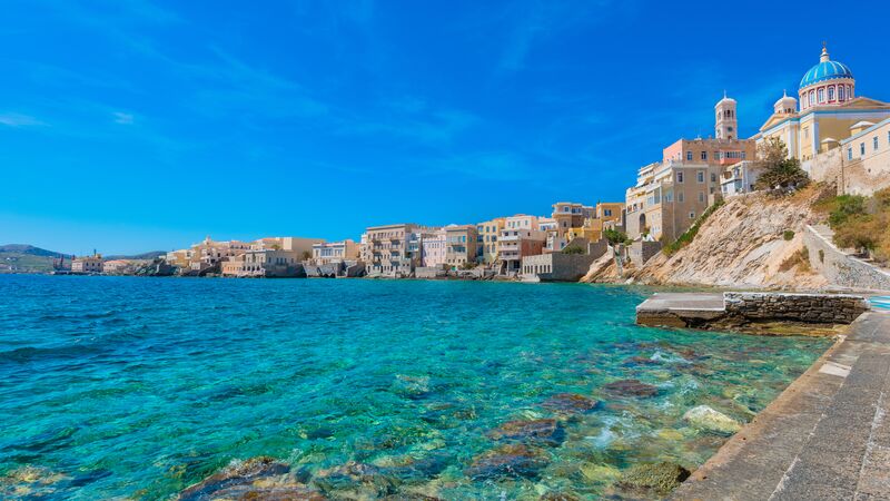 Houses and buildings along the crystal clear water's edge on an island in Greece. 