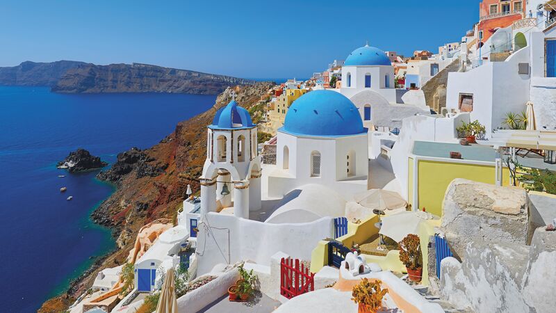 White-washed and blue-domed houses on the side of a mountain on a Greek island.