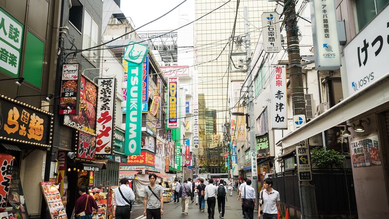 The bustling, crowded street of an anime district with brightly coloured signs. 