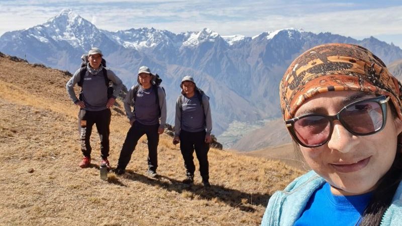 A woman takes a selfie with three Peruvian porters in the background