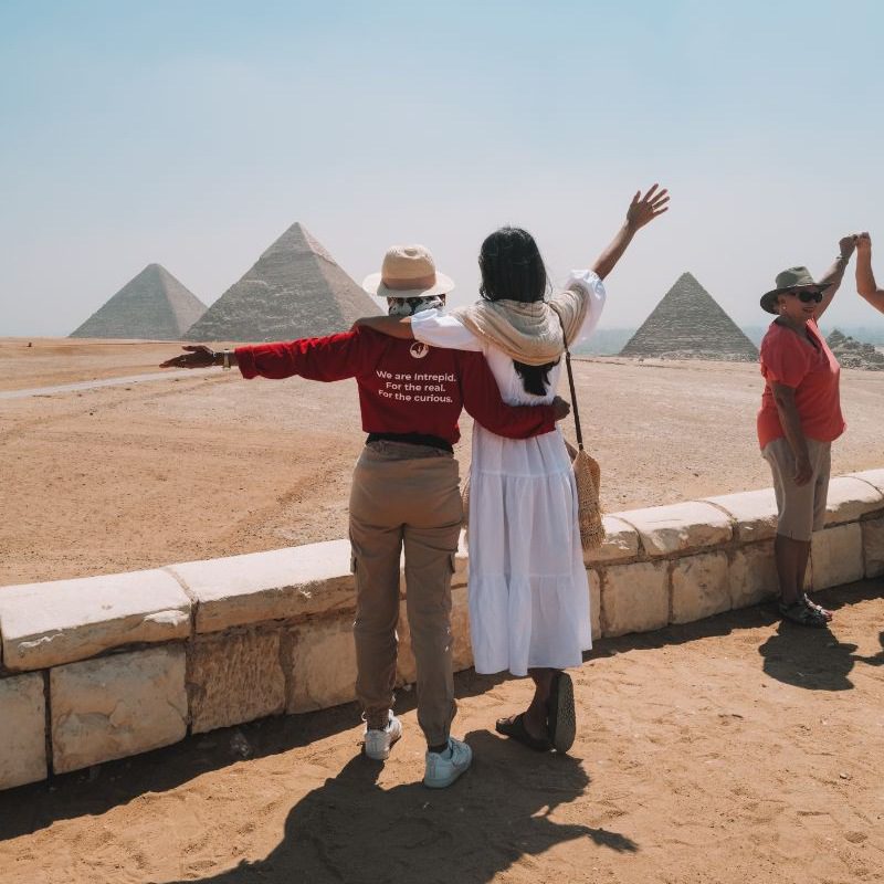 Two woman - one wearing a red t-shirt, the other in a white dress - with their arms around each other at the pyramids in Egypt