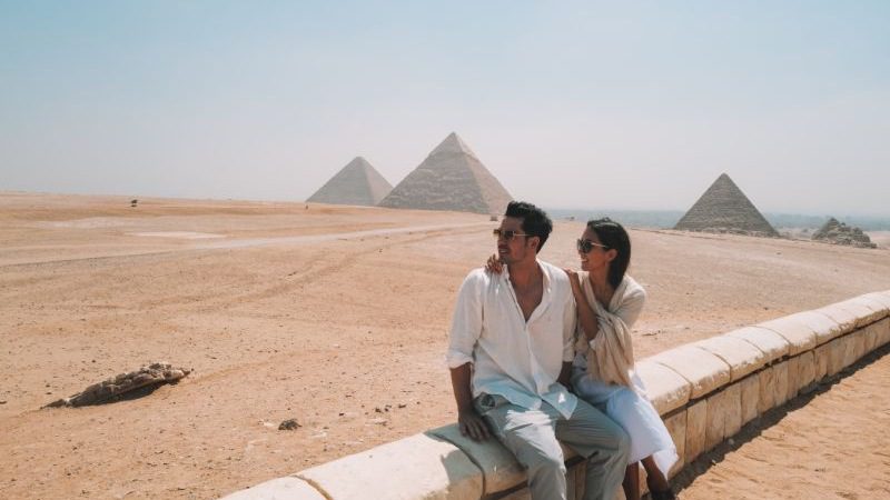 A happy couple sitting on a wall looking at the pyramids in Egypt