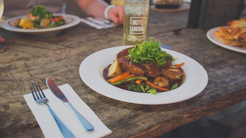 A wooden table laden with colourful food beside knives and forks.