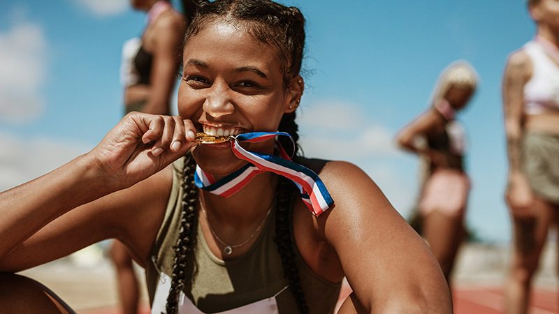 Woman biting an Olympic gold medal after winning a track event.