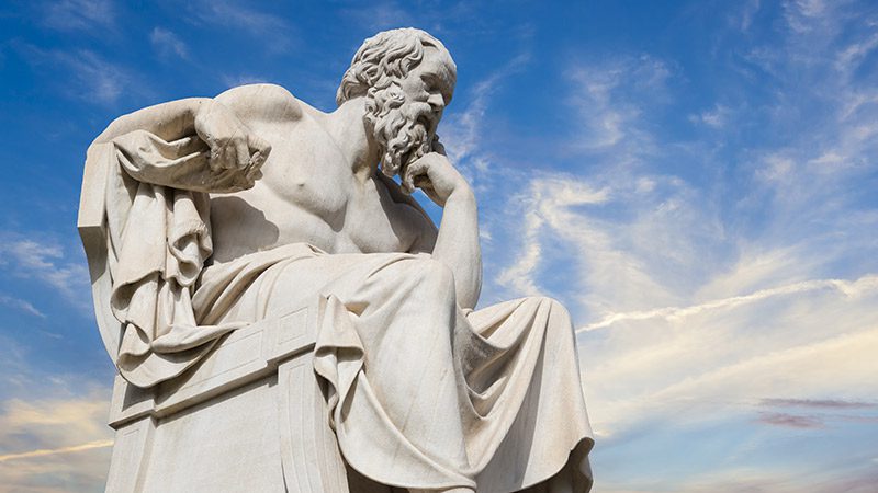 A stone statue of an Ancient Greek philosopher with blue sky in the background.