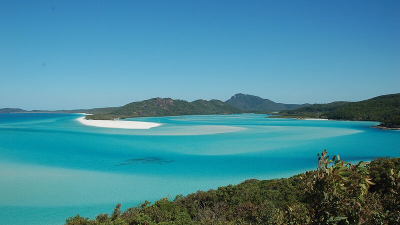 A paradise-like Airlie Beach landscape with crystal clear waters under a blue, sunny sky.