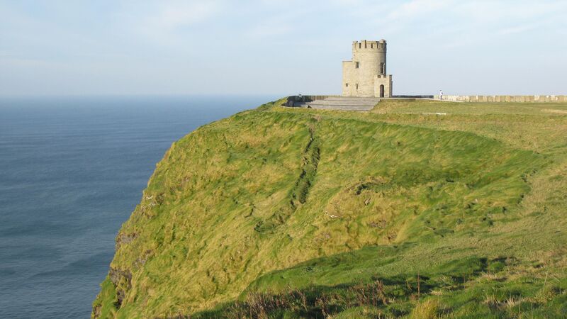 A castle stands on the green, grassy edge of the Cliffs of Moher. 
