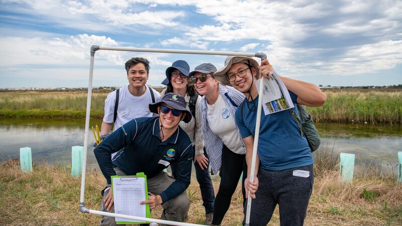 A group of people holding a frame and smiling near a creek