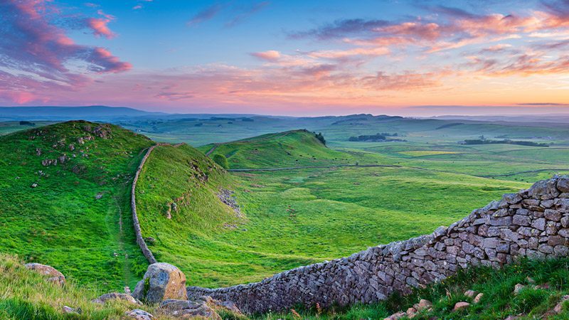 A stretch of Hadrian's Wall in England beside green hills at sunset.