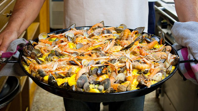 A person holding a tray of paella