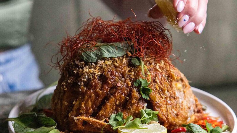 A heaped plate of food with lemon being squeezed over it.