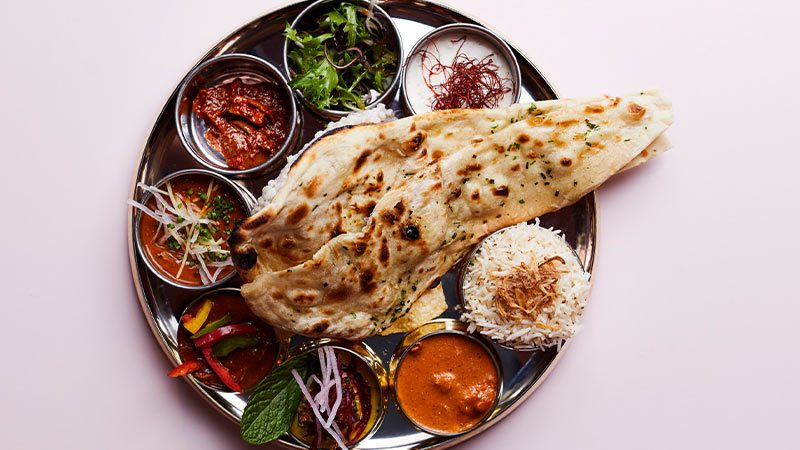 A plate full of curry samples, rice, green garnish and naan bread.