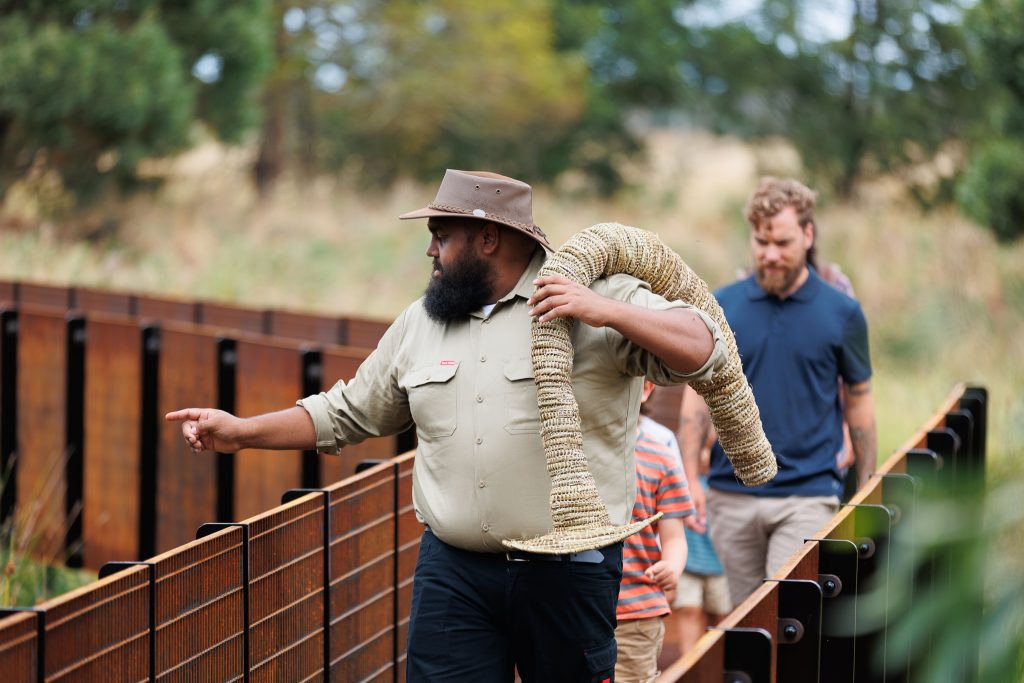 A man holding an eel trap walking across a bridge