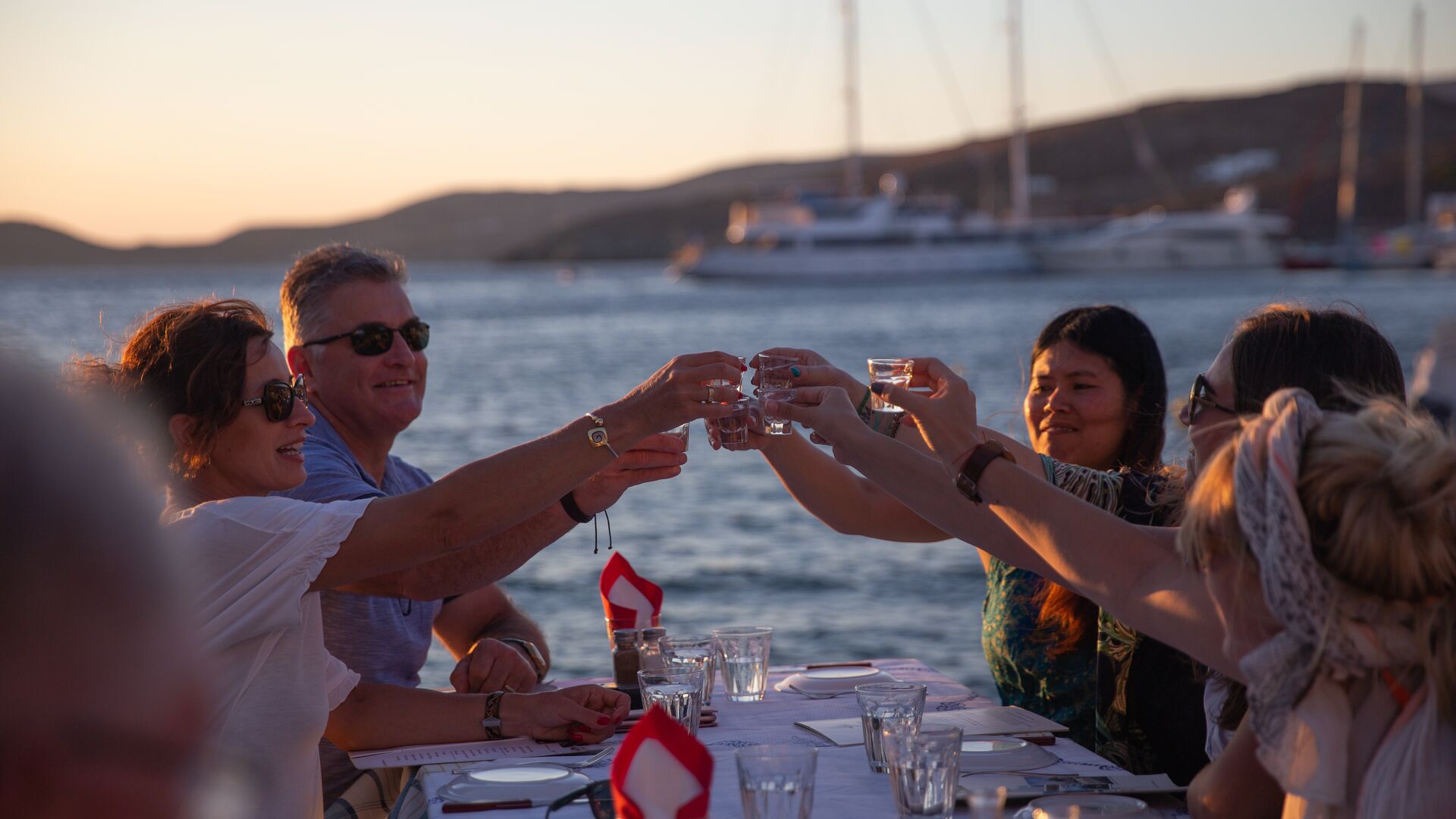 A group of travellers raising a toast with shot glasses filled with ouzo.