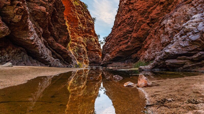 The red rock walls of Simpsons Gap with a clear river of water running through it. 