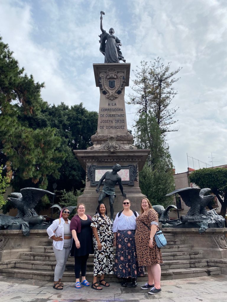Five women pose in front of a statue in Mexico