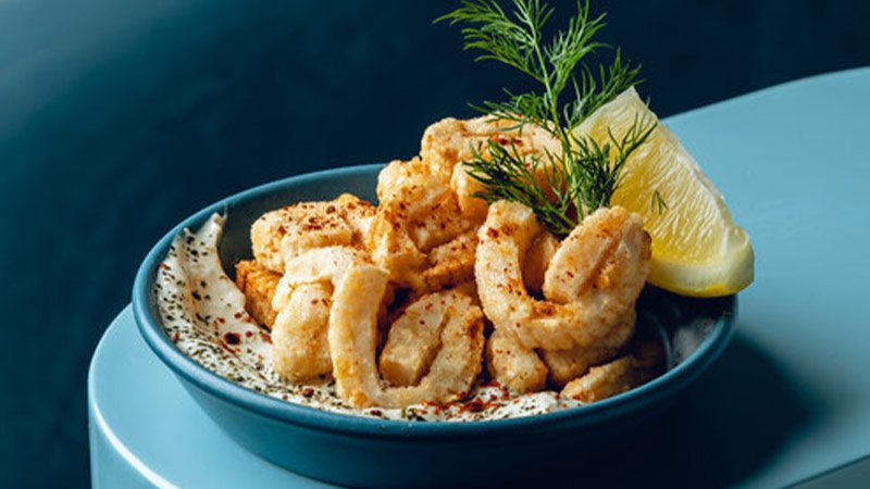 A small serving of calamari accompanied by a lemon wedge and some garnish. 
