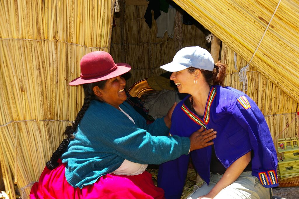 A traveller and Uru woman smile at eachother infront of a reed hut on the Uros Islands, Lake Titicaca, Peru.