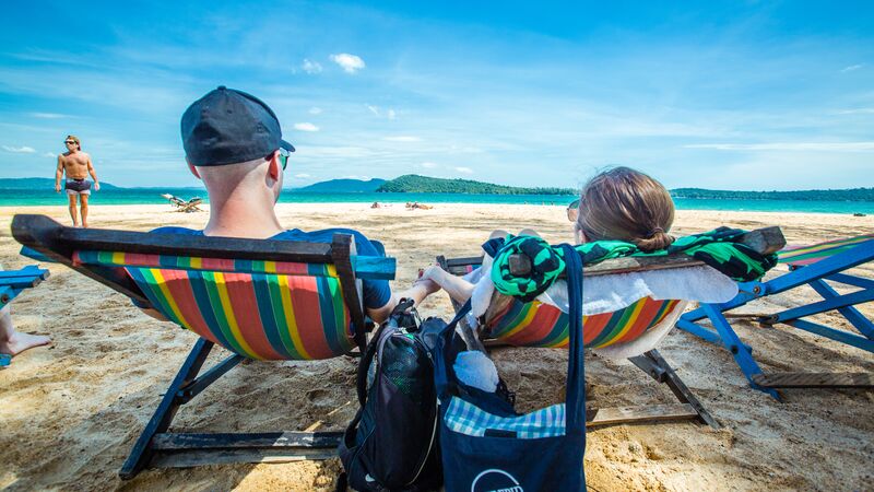 Two travellers lying on beach chairs on a beach in Sihanoukville under clear skies. 