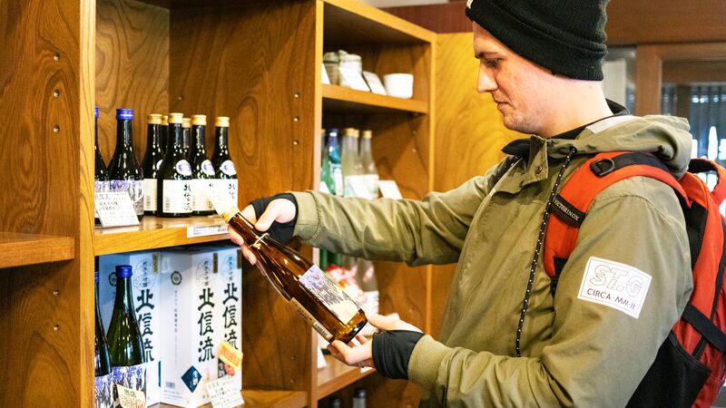 A man in a black knitted hat looking at a bottle of sake in Japan