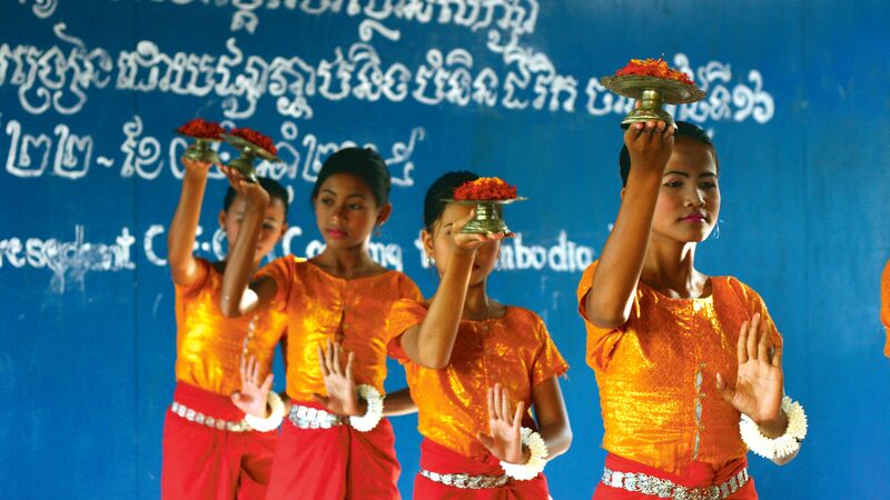 A group of Cambodian women dancing a traditional routine dressed in bright orange.