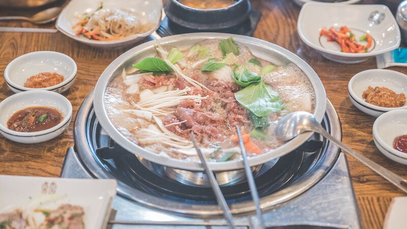 Meat bubbling away on a stove with spices and vegetables around it