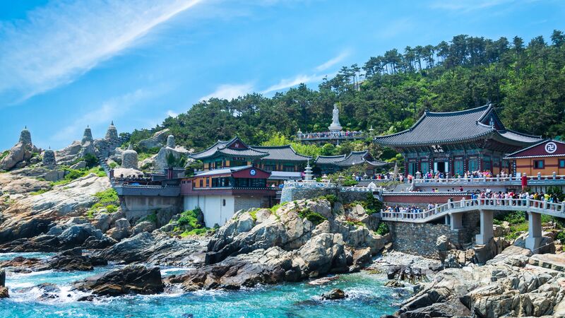 A traditional temple perched along the coast of Busan on a sunny day. 